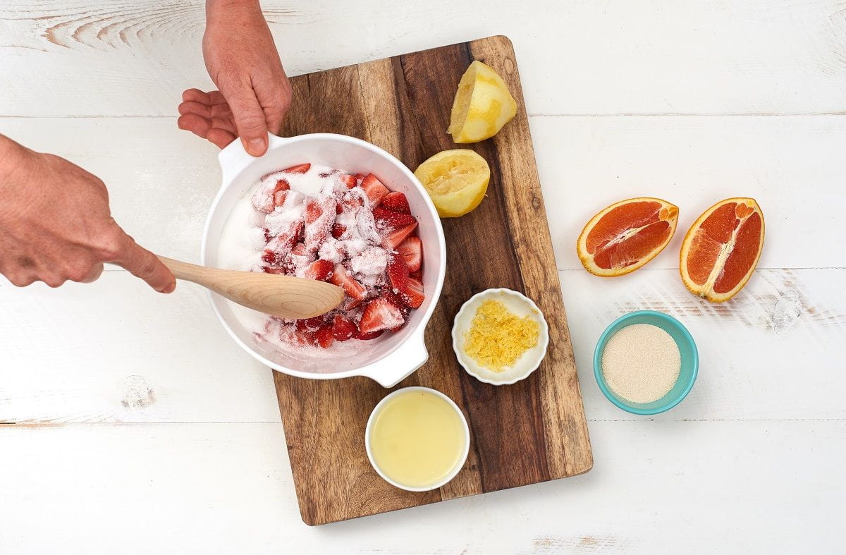 mixing sugar and strawberries together in bowl on cutting board